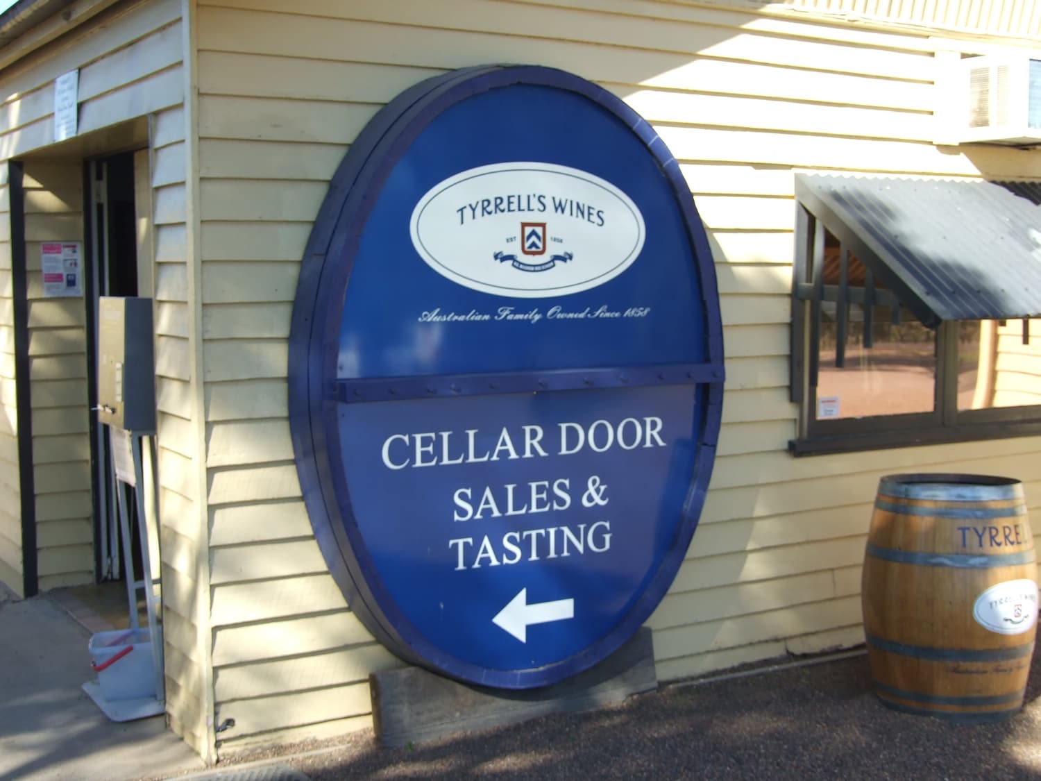 Ein blaues ovales Schild „Cellar door sales & tasting“ vor dem holzverkleideten Weingut Tyrrell’s in Pokolbin