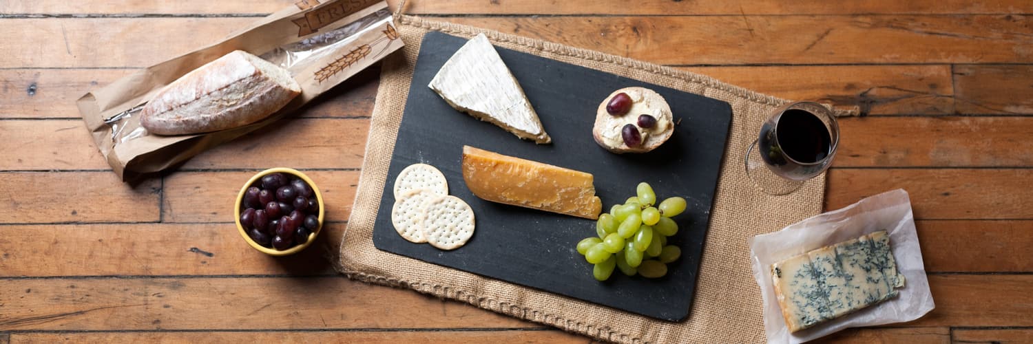 Eine Schieferplatte mit Weich- und Hartkäse, Crackern, Oliven und grünen Trauben